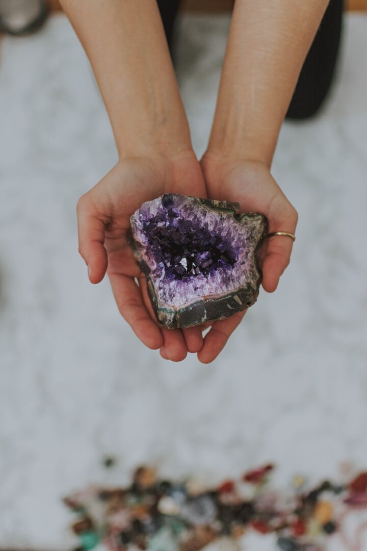 A closeup shot of a girl holding a multicolored rock in her hands over a white surface