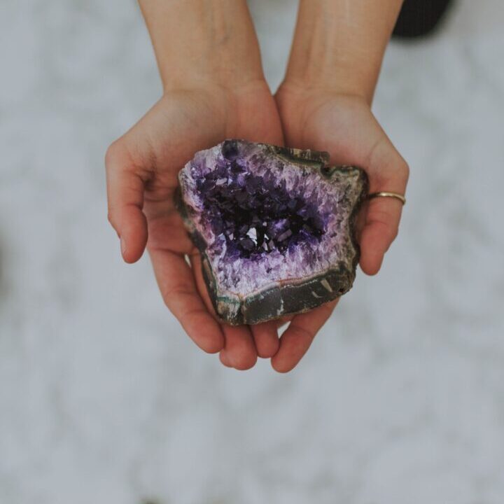 A closeup shot of a girl holding a multicolored rock in her hands over a white surface
